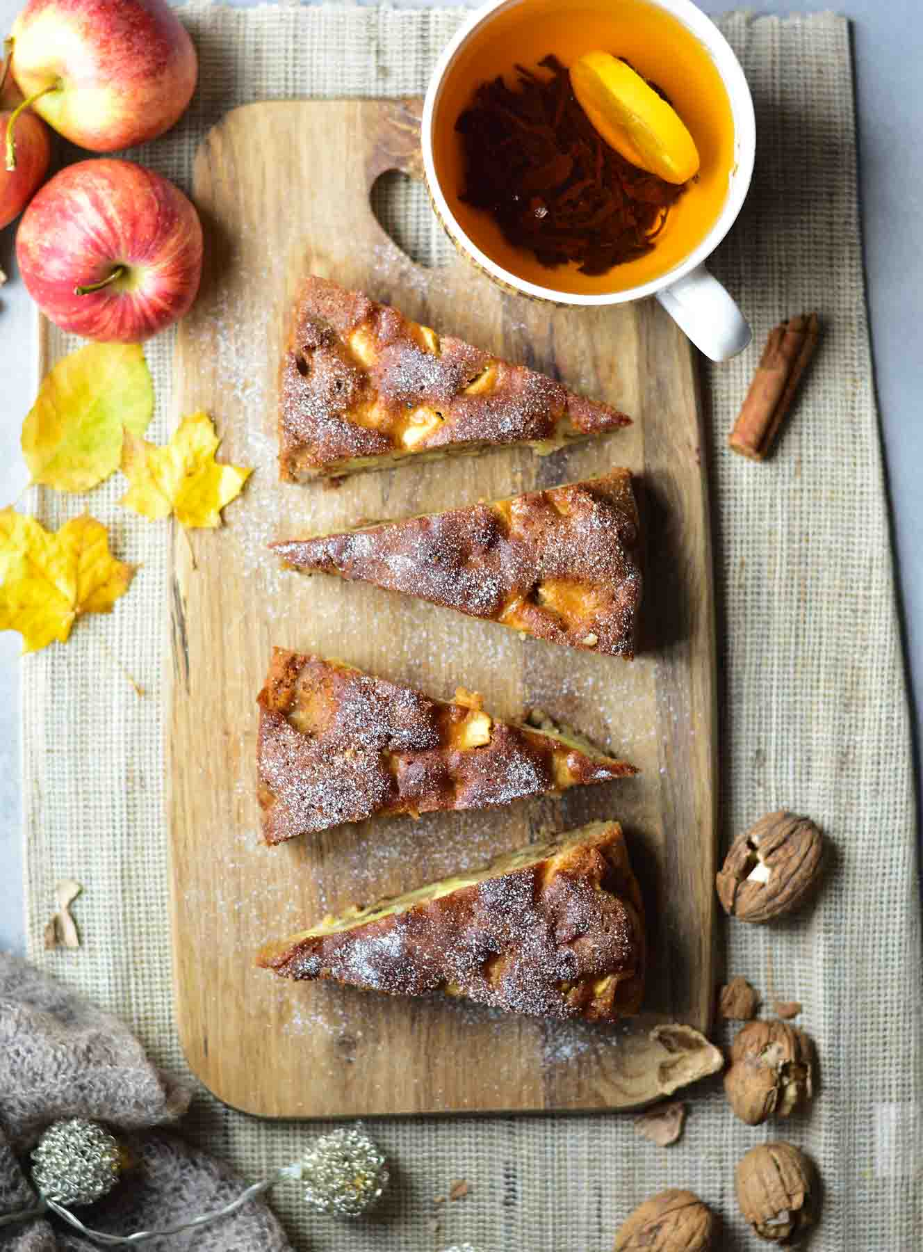 Apple walnut cake with honey on a wooden board. Apples and tea in the background.