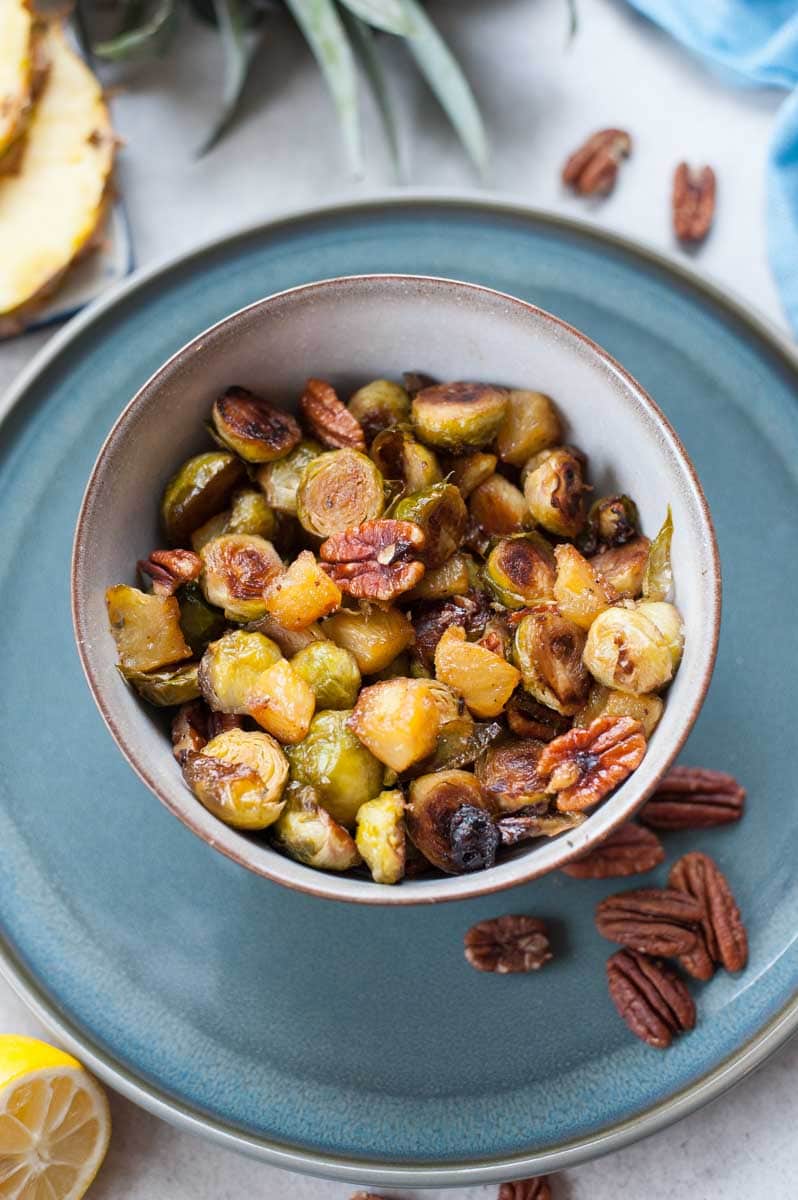 Roasted brussel sprouts with pineapple and pecans in a grey bowl.