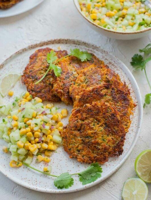 Sweet potato zucchini fritters with corn cucumber salsa on a white plate.