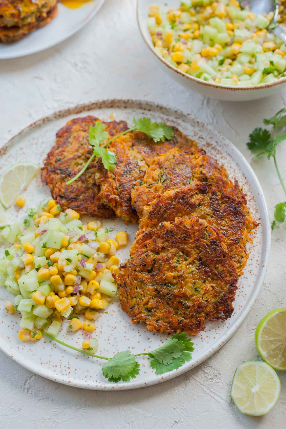 Sweet potato zucchini fritters with corn cucumber salsa on a white plate.