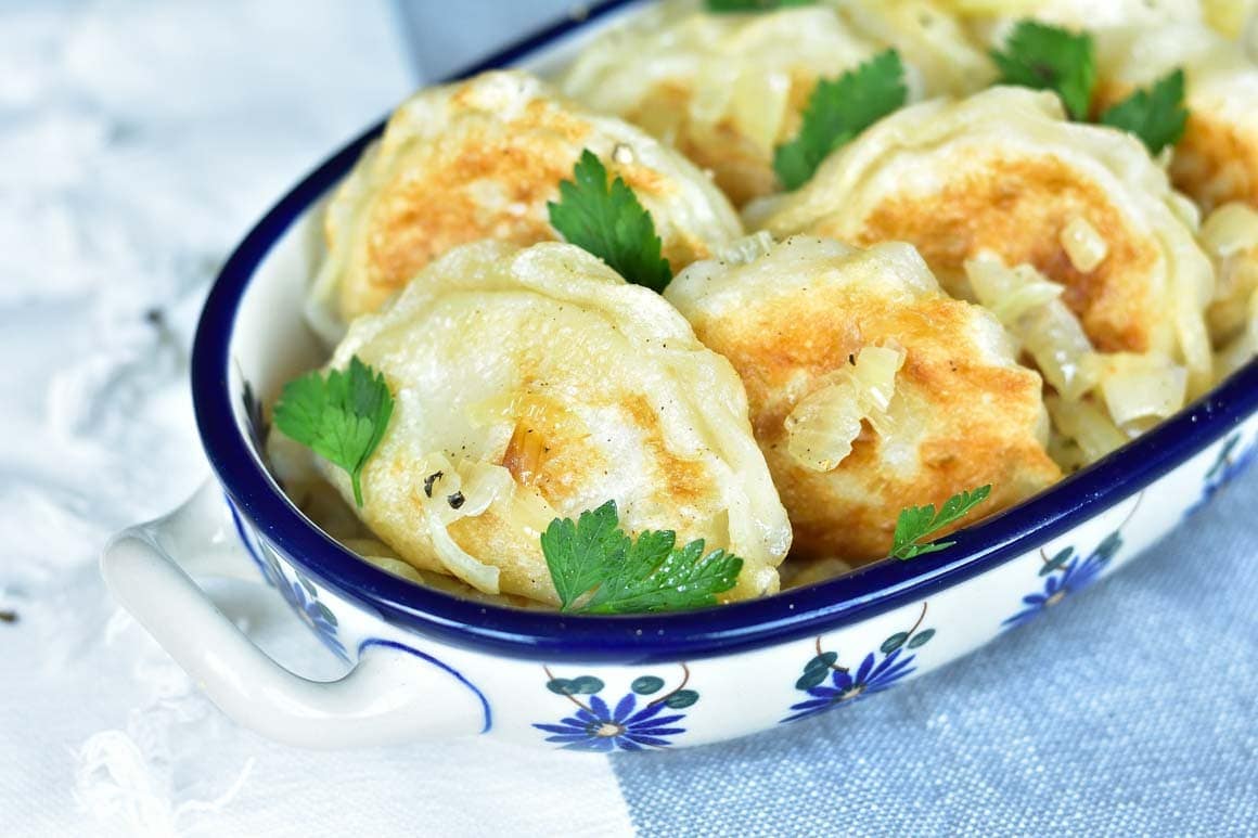 Pierogi ruskie in a blue-white dish, topped with sauteed onion and parsley.