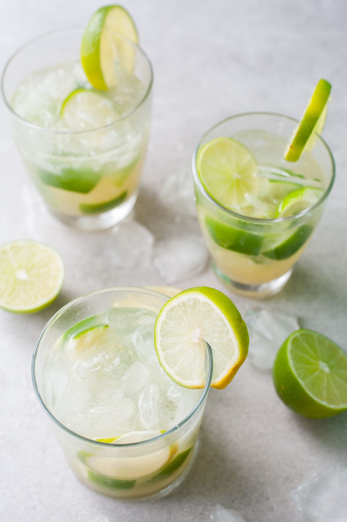 Three glasses with caipirinha. Limes and ice around the glasses.