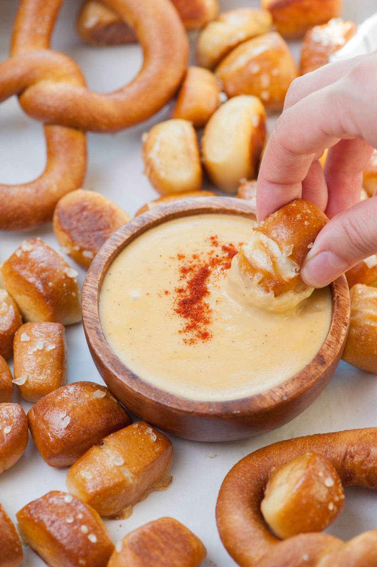 A soft pretzel bite is being dipped into beer cheese dip. More pretzel bites around the bowl.