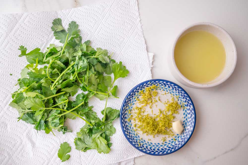 Cilantro on paper towels. Grated lime zest and garlic on a plate. Lime juice in a bowl.