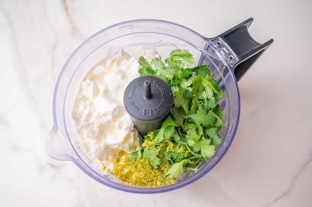 All the ingredients for Cilantro Lime Crema in a food processor bowl.