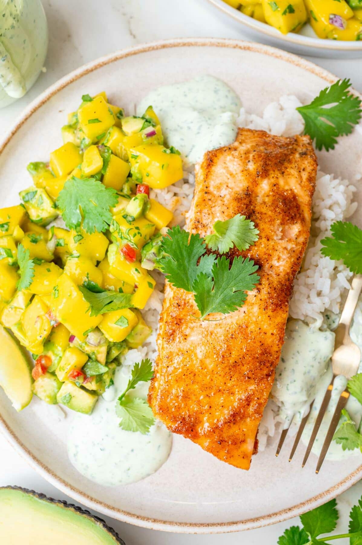 An overhead photo of salmon rice bowls consisting of baked salmon, mango avocado salsa, rice, and cilantro lime crema.