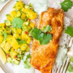 Baked salmon with mango avocado salsa, rice, and cilantro lime crema on a beige plate.