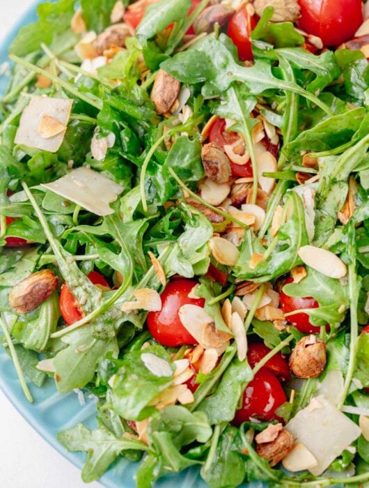 A close up photo os arugula salad on a blue plate.