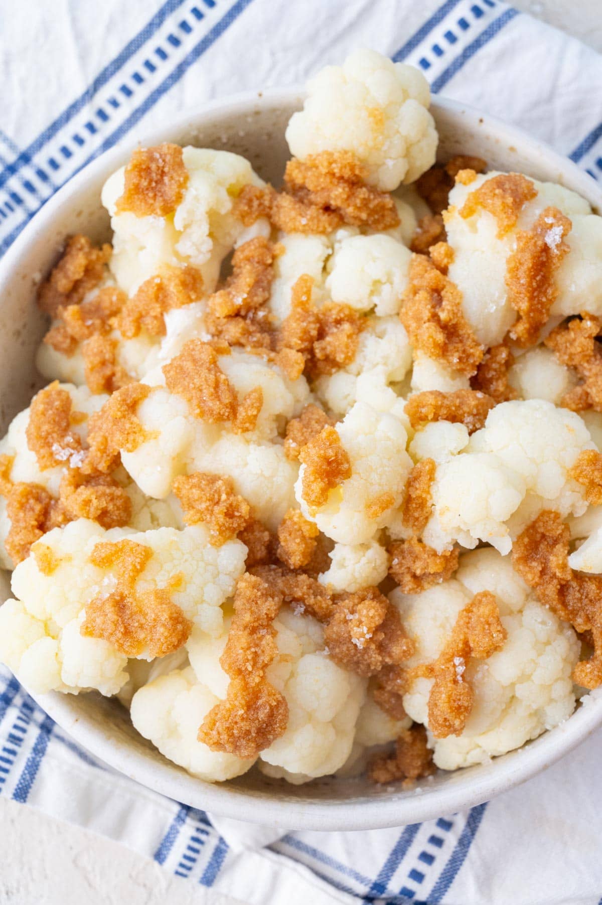 Steamed cauliflower florets topped with fried buttered breadcrumbs in a white bowl.