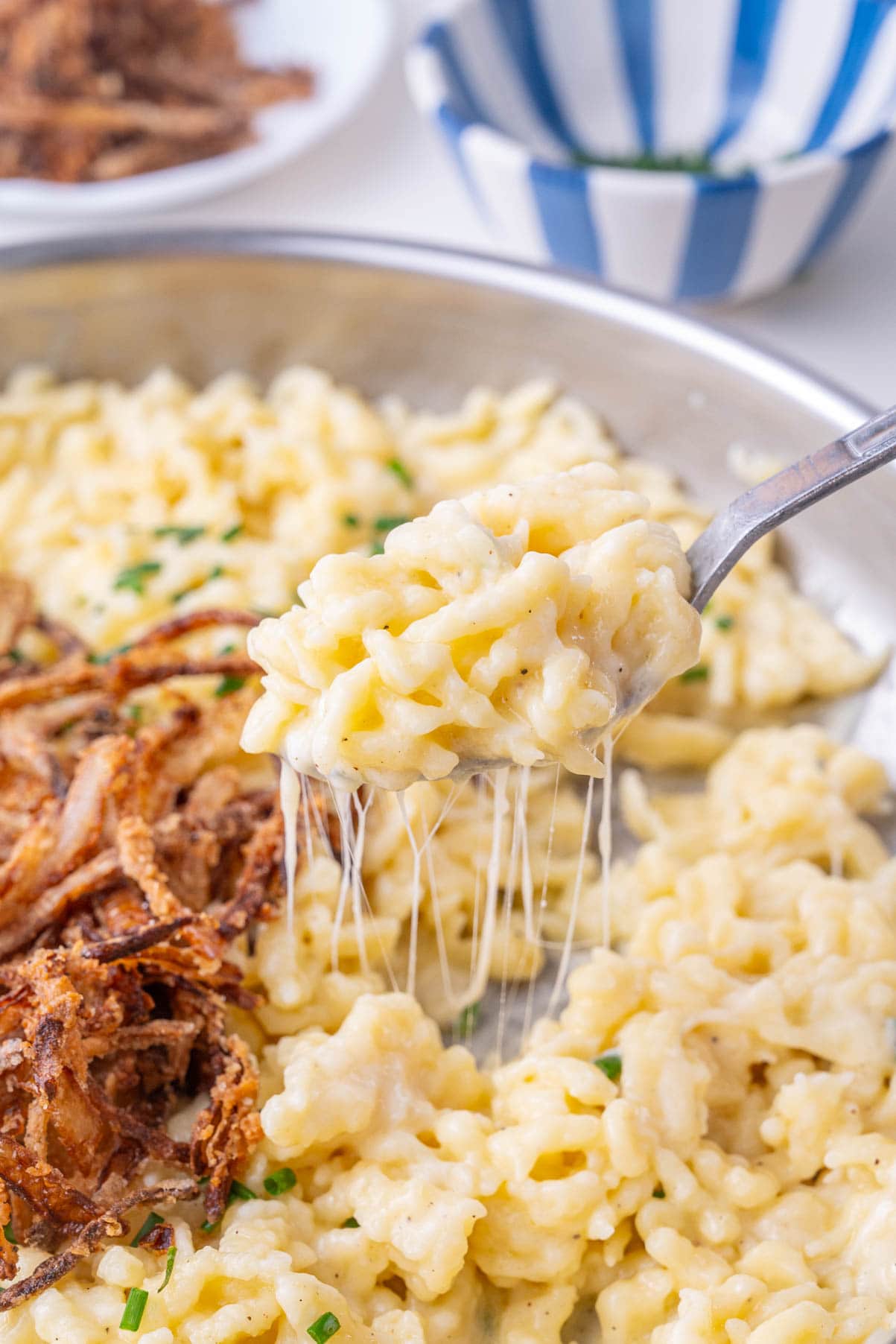 Käsespätzle on in a frying pan and on a fork topped with crispy onions.
