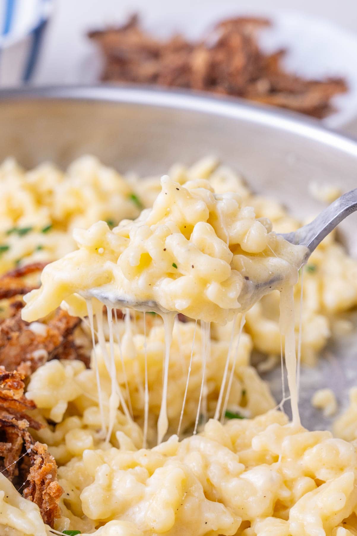 A close up photo of cheese pull and Käsespätzle on a spoon being grabbed from the frying pan.