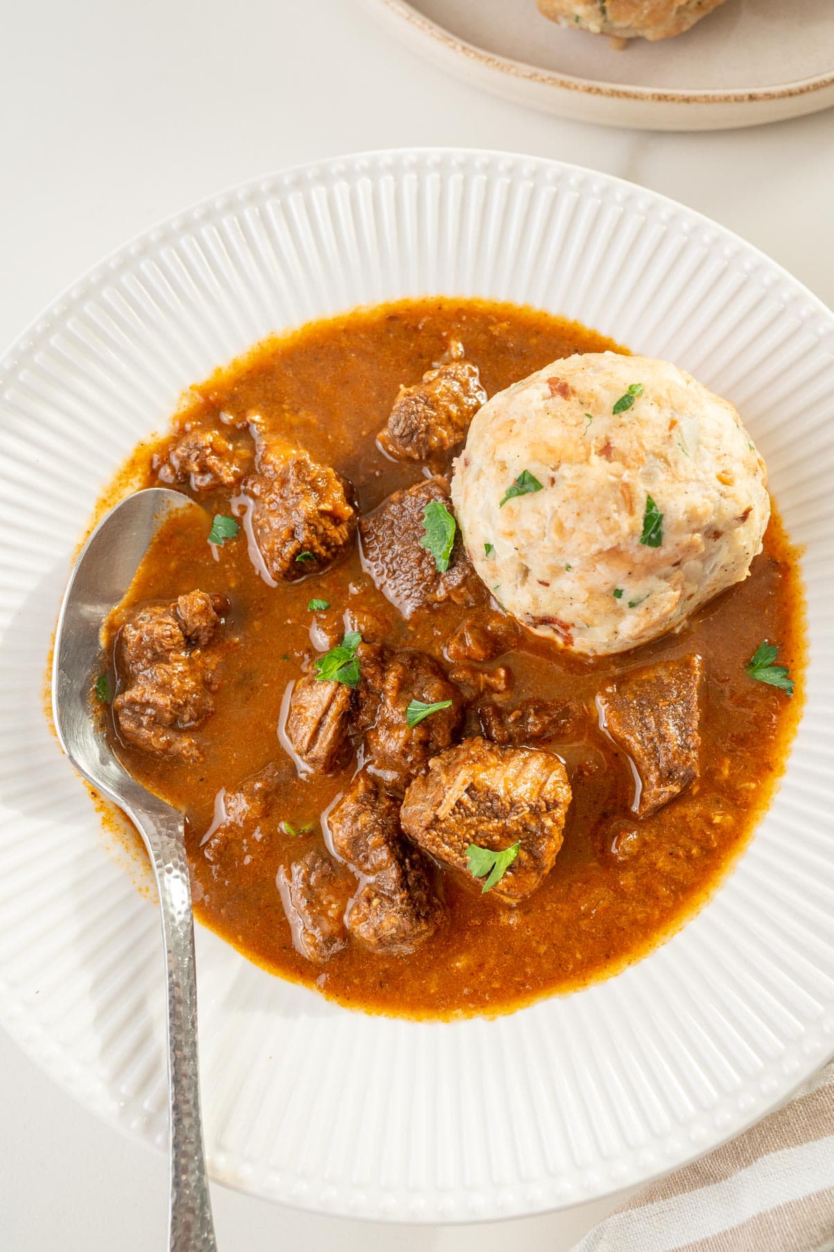 Viennese Goulash in a white plate with Semmelknödel on the side.