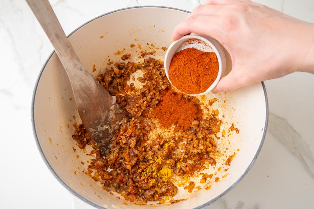 Paprika is being added to a pot with caramelized onions.