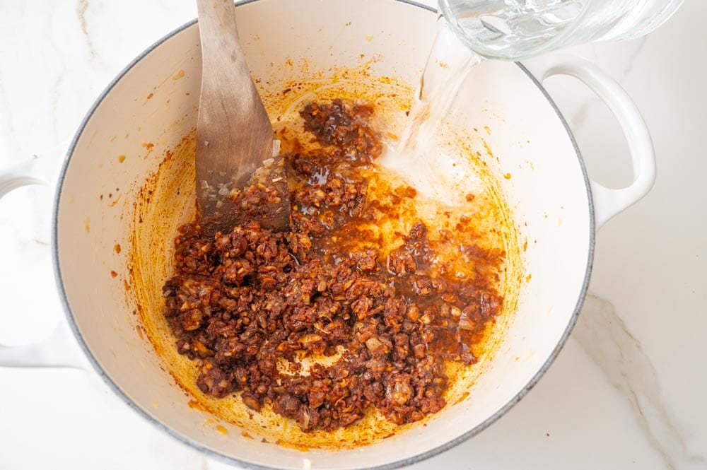 Water is being added to a pot with caramelized onions and spices.