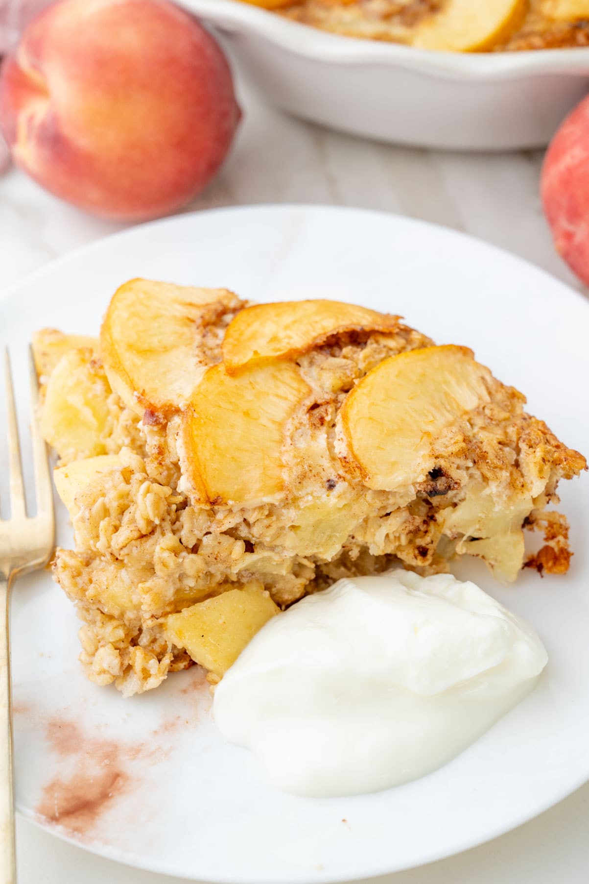 A piece of baked peach oatmeal on a white plate with a dollop of yogurt.