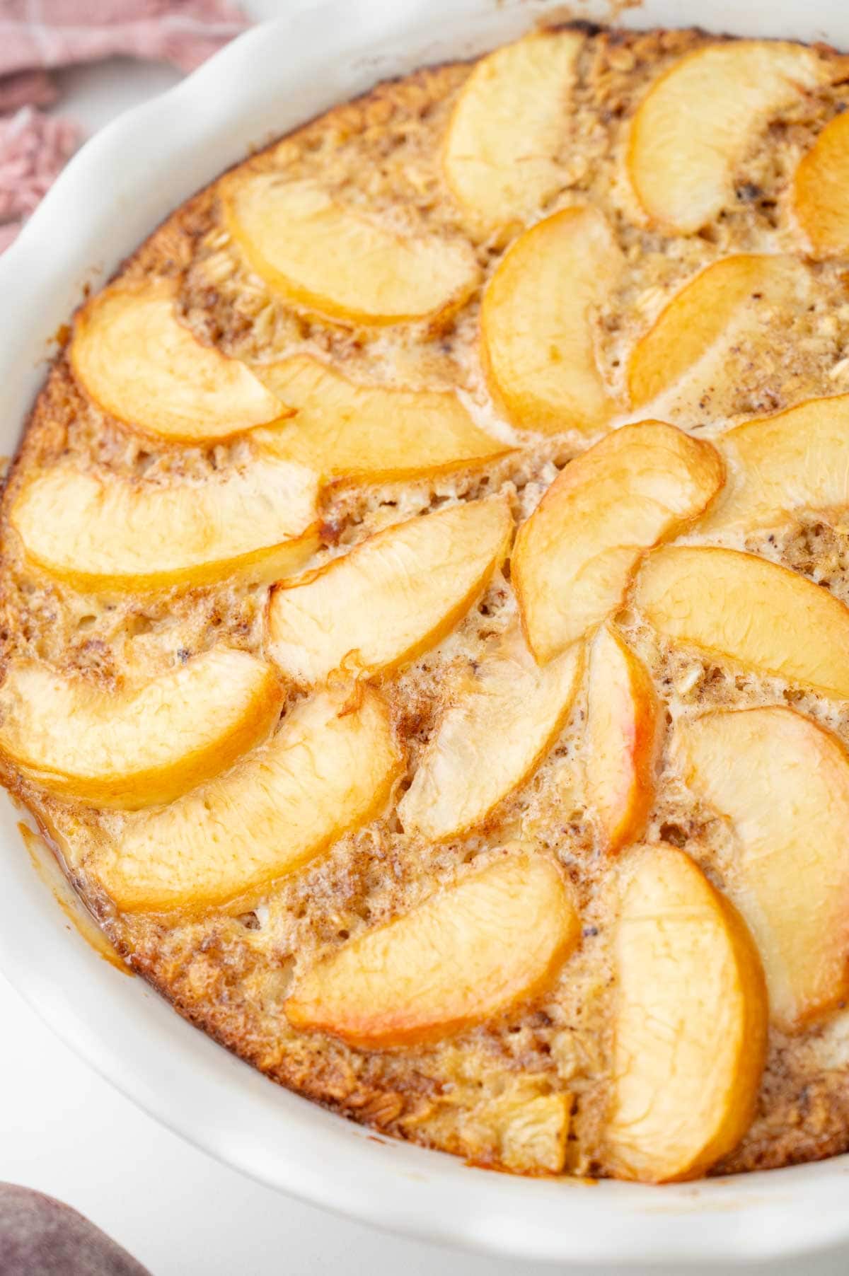 A close up photo of baked peach oatmeal in a white baking dish.