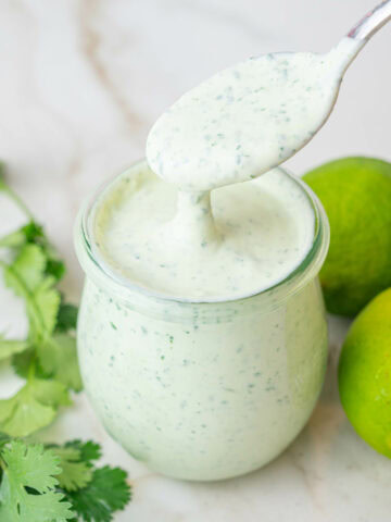 Cilantro lime crema in a jar. Cilantro and limes in the background.