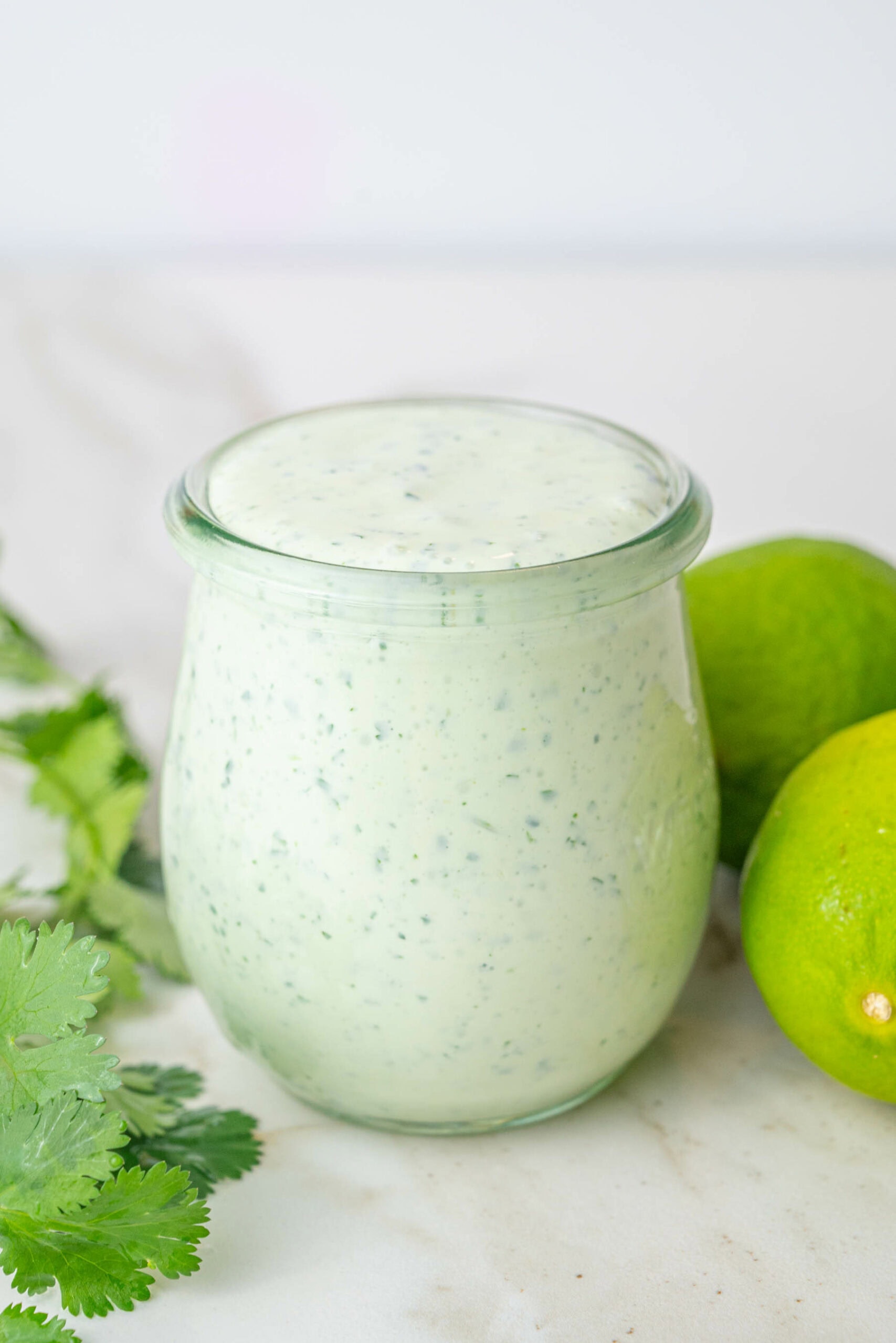 Cilantro Lime Crema in a small jar surrounded with limes and cilantro leaves.