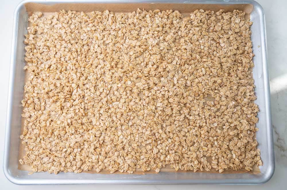 Oats coated in melted butter and maple syrup on a baking sheet.