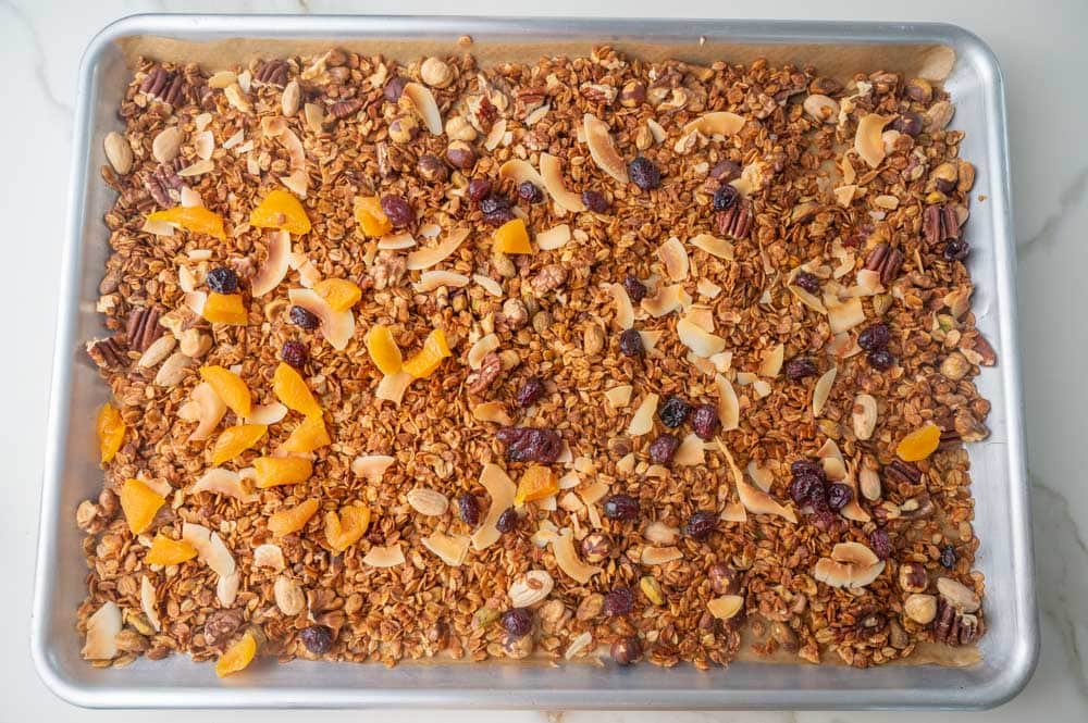 Baked granola with mixed nuts, coconut chips, dried apricots, and cranberries on a baking sheet.