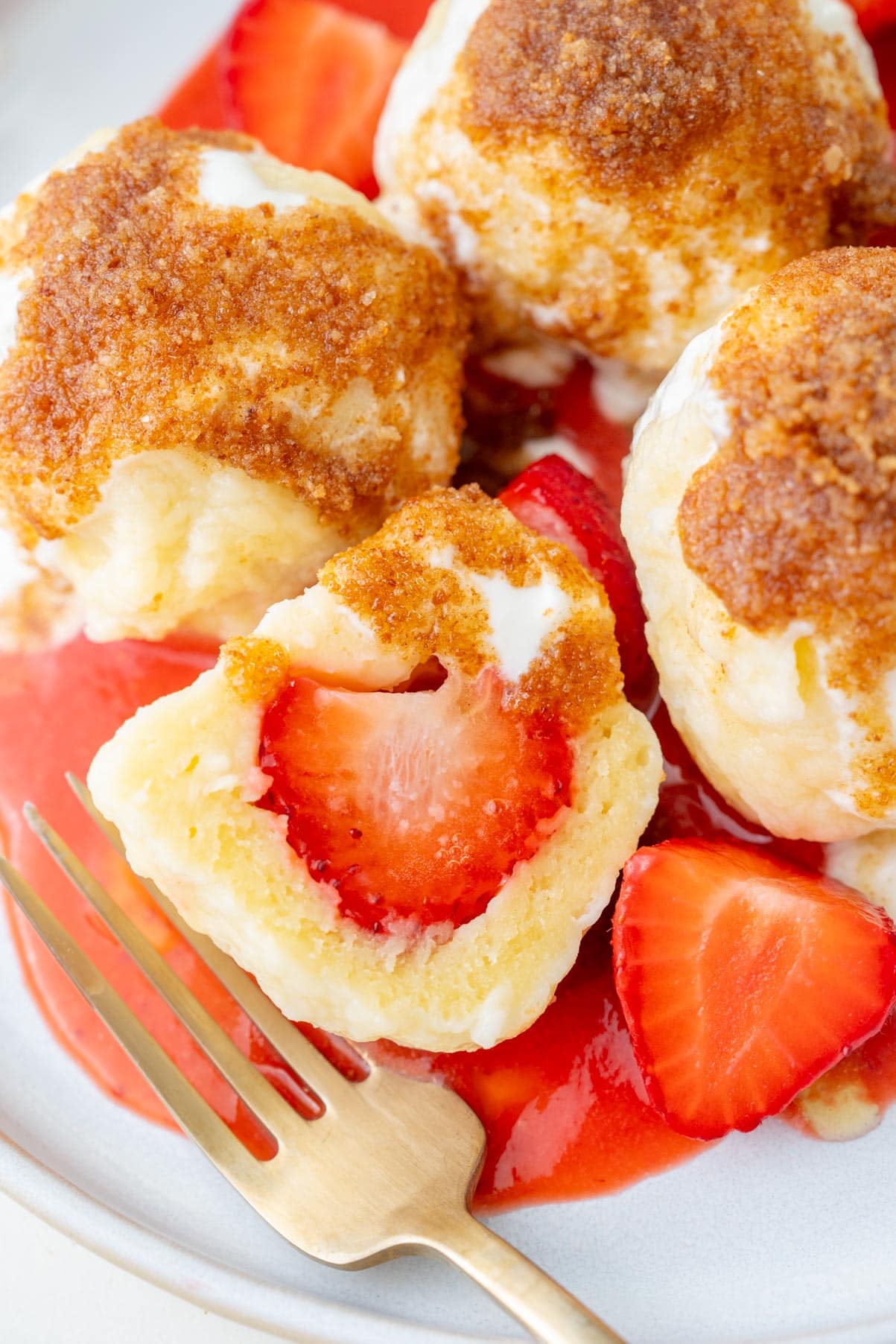 A close-up photo of Polish strawberry dumplings served with fried breadcrumbs, sweetened sour cream, and strawberry sauce on a white plate.