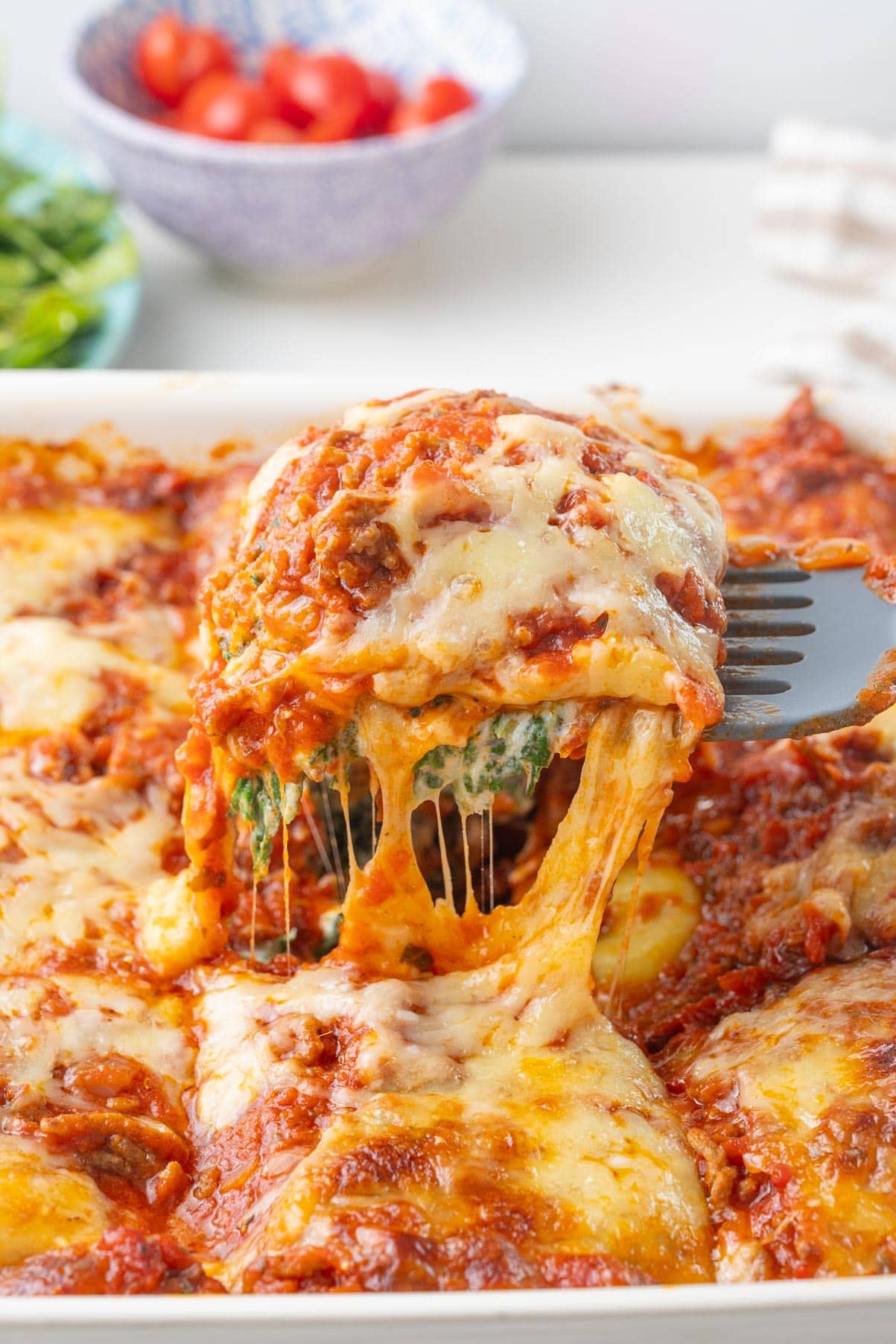 A square serving of ravioli lasagna is being lifted on a spatula from a casserole dish.