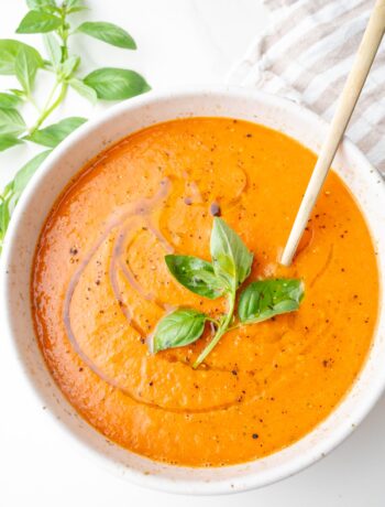 Roasted tomato soup in a white bowl topped with basil leaves and drizzled with olive oil.