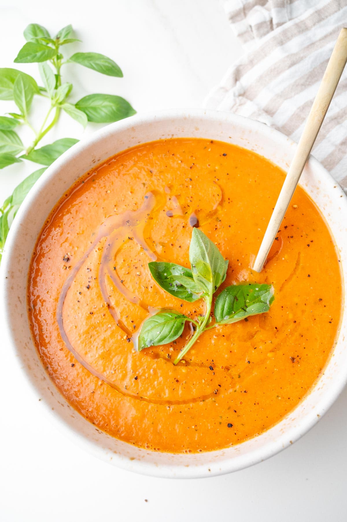 Roasted Tomato Soup in a white bowl drizzled with olive oil and topped with basil leaves.
