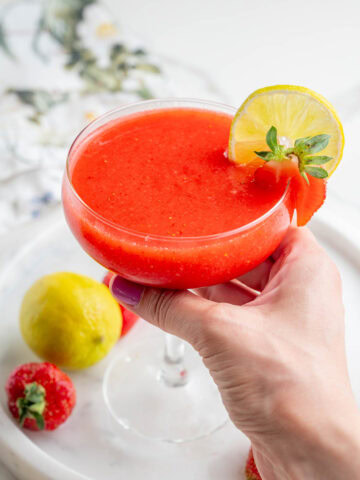 One glass with a strawberry margarita is being held in a hand.