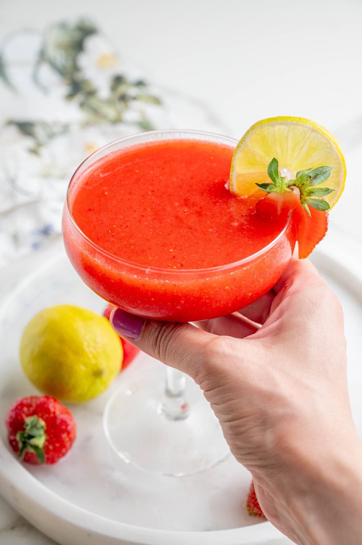 One glass with a strawberry margarita is being held in a hand.