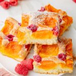 Apricot raspberry sponge cake squares on a white plate.