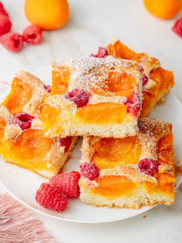 Apricot raspberry sponge cake squares on a white plate.