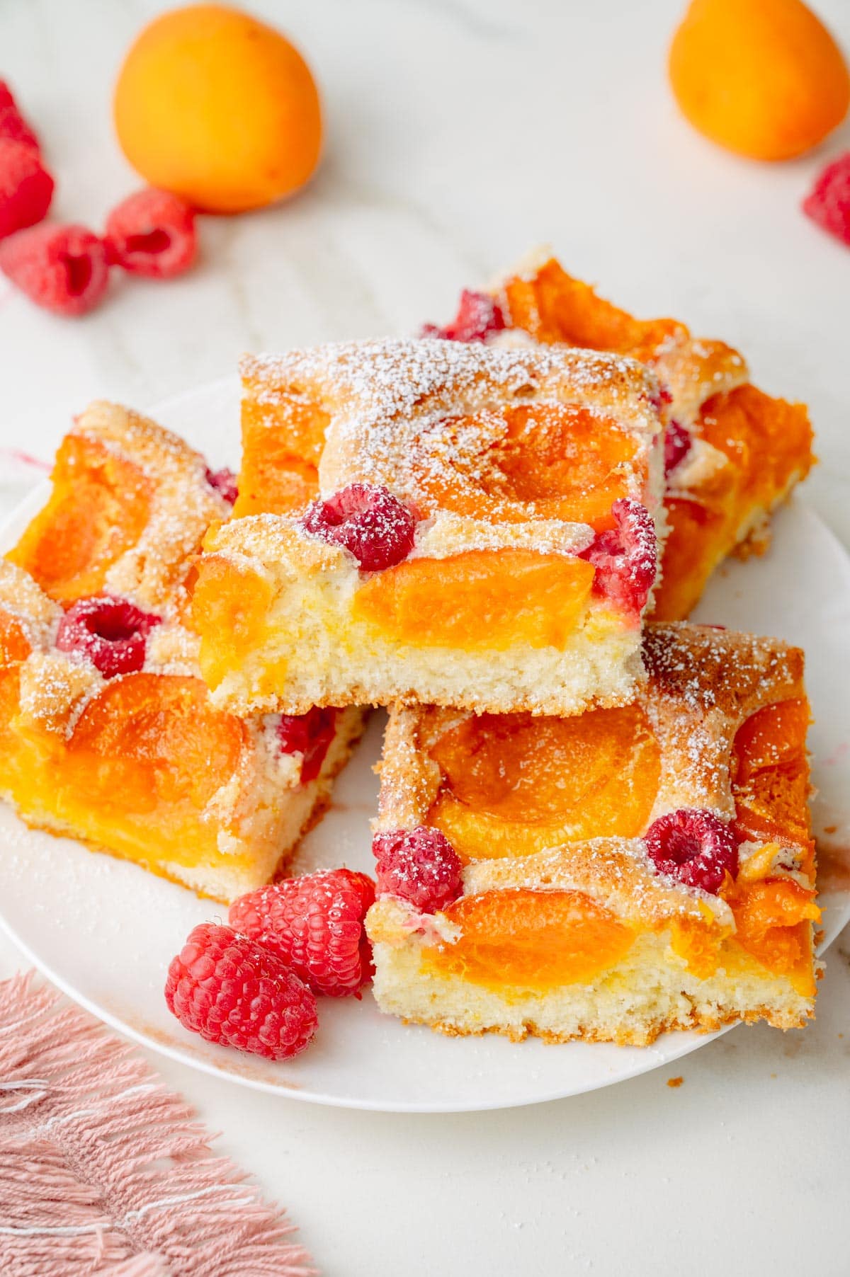 Squares of Apricot Raspberry Sponge Cake on a white plate.