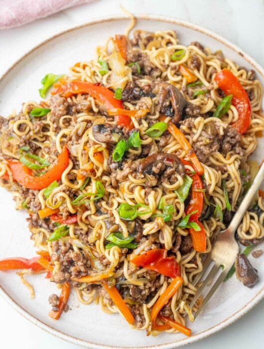 Ground beef noodles with vegetables on a white plate.