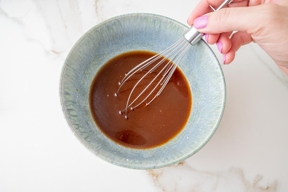 Sauce for noodles is being whisked in a bowl.