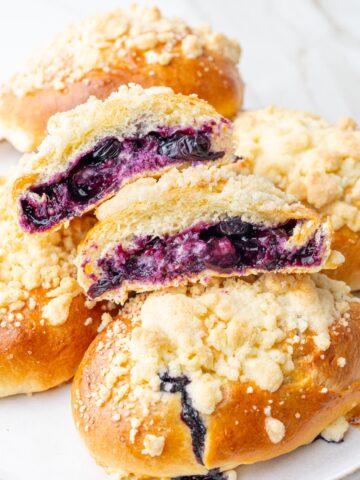 Jagodzianki Polish buns on a white plate. One bun is cut in half showing blueberry filling.