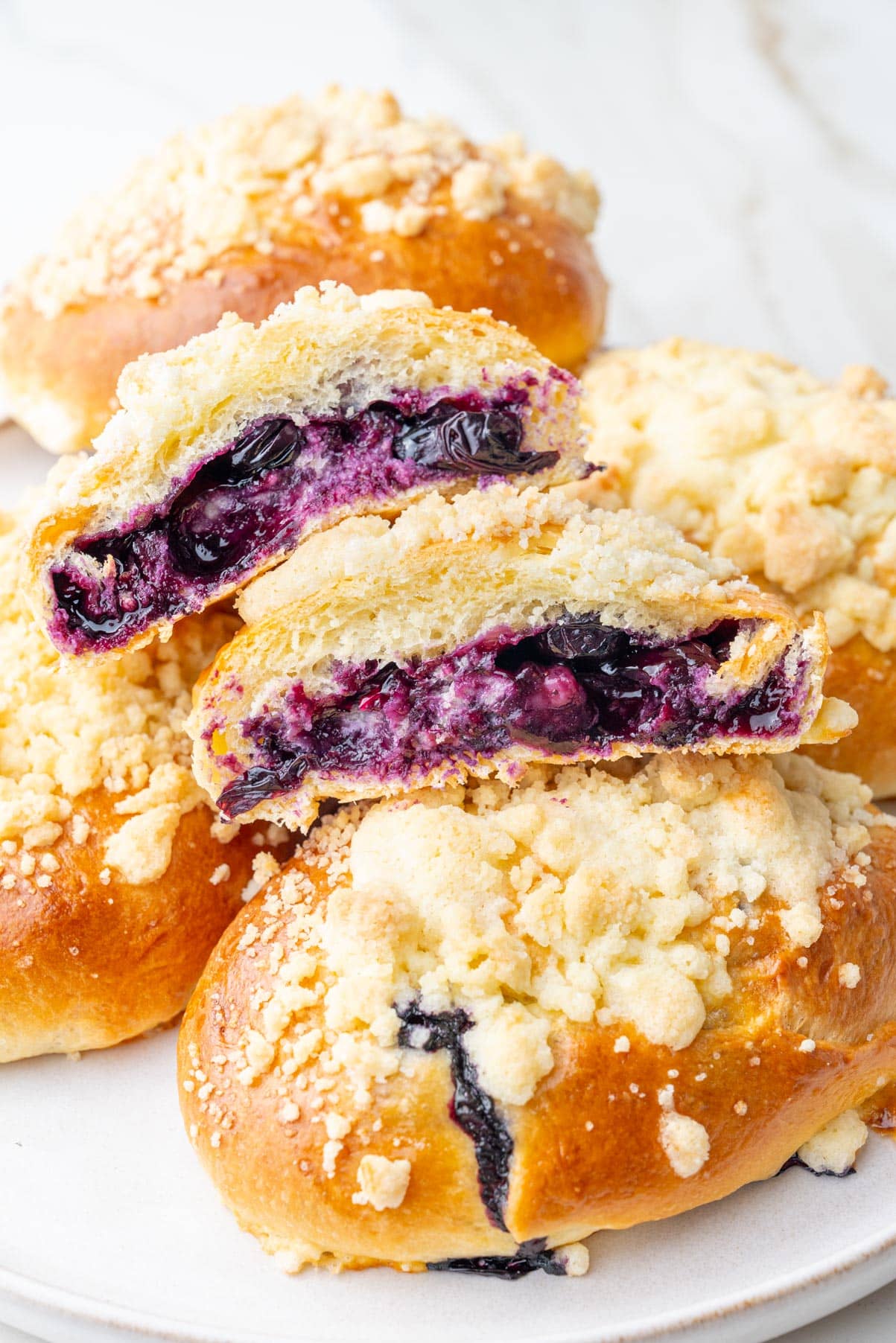 Jagodzianki Polish buns on a white plate. One bun is cut in half showing blueberry filling.