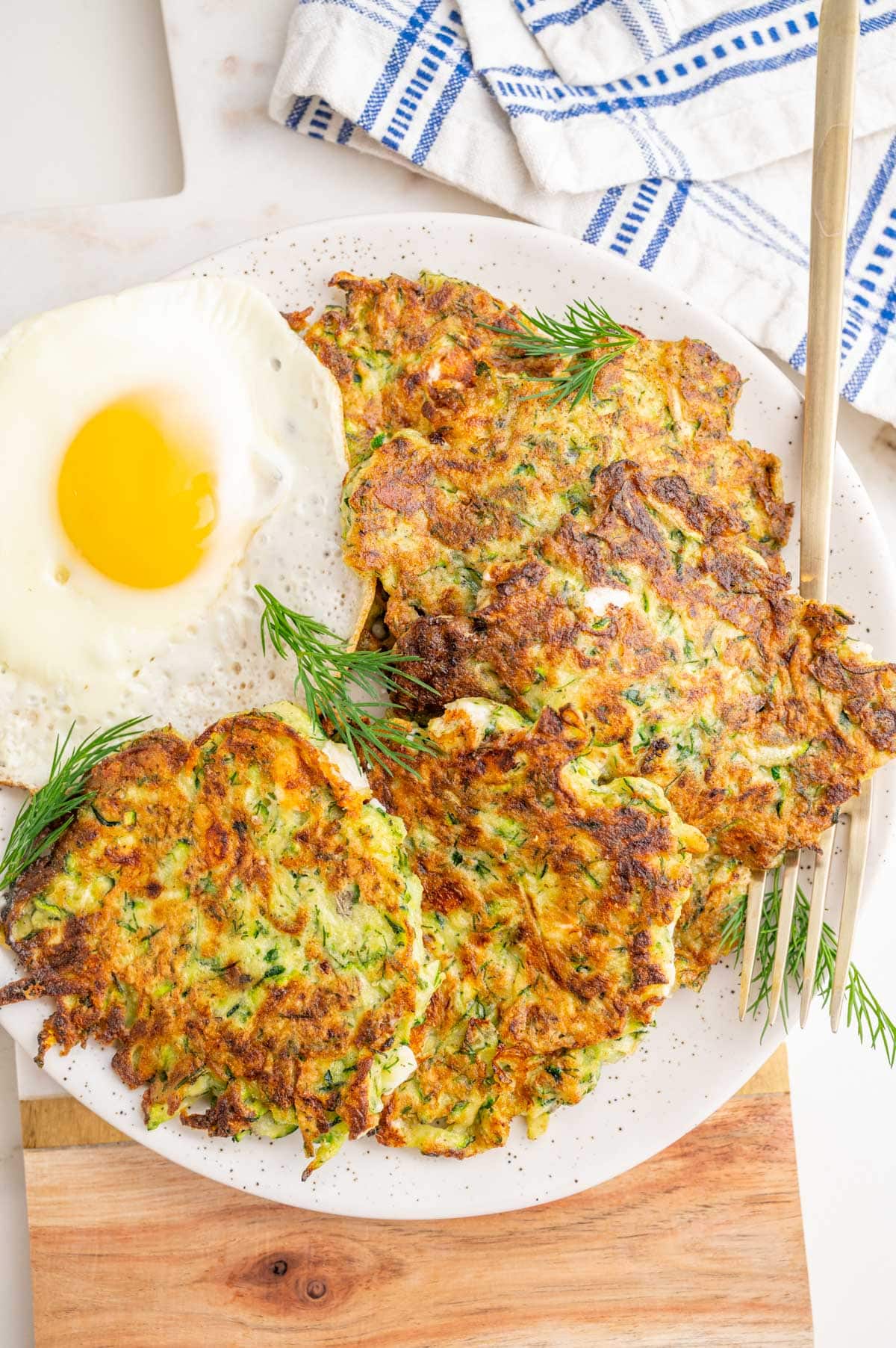 Zucchini fritters on a white plate with sunny-side-up egg on the side.