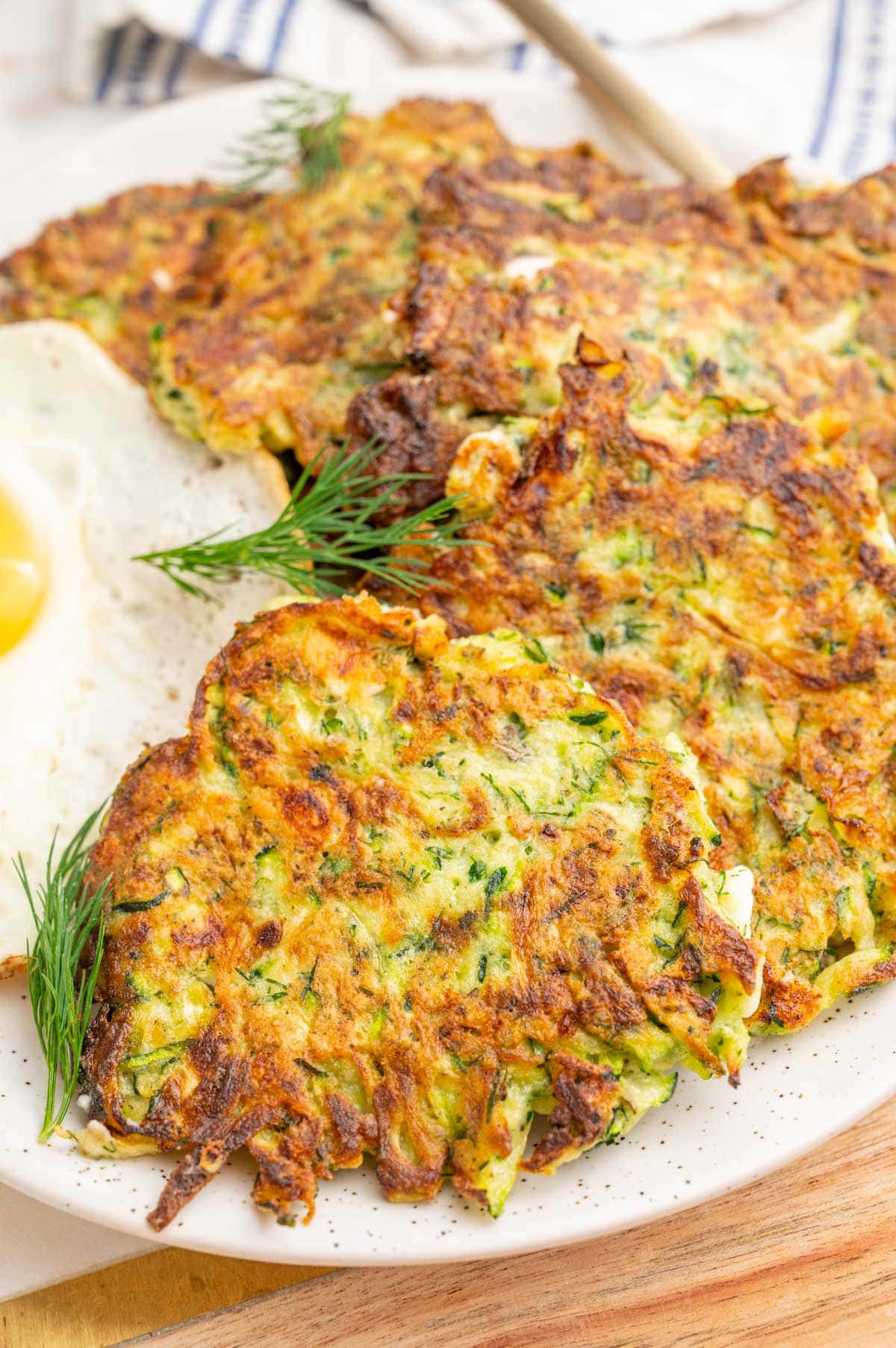 A close up photo of zucchini fritters with feta and dill on a white plate.