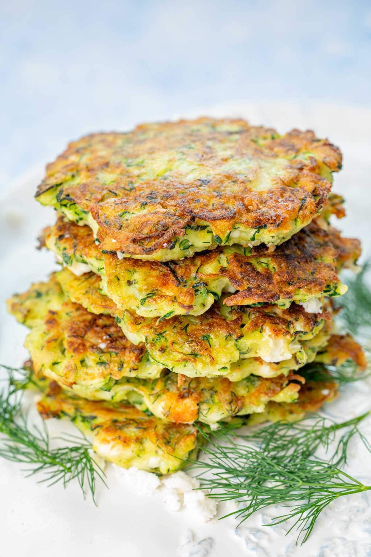 A stack of zucchini fritters with feta and dill on a white plate.