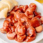 Currywurst on a white plate. Bread rolls and beer in the background.