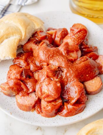 Currywurst on a white plate. Bread rolls and beer in the background.