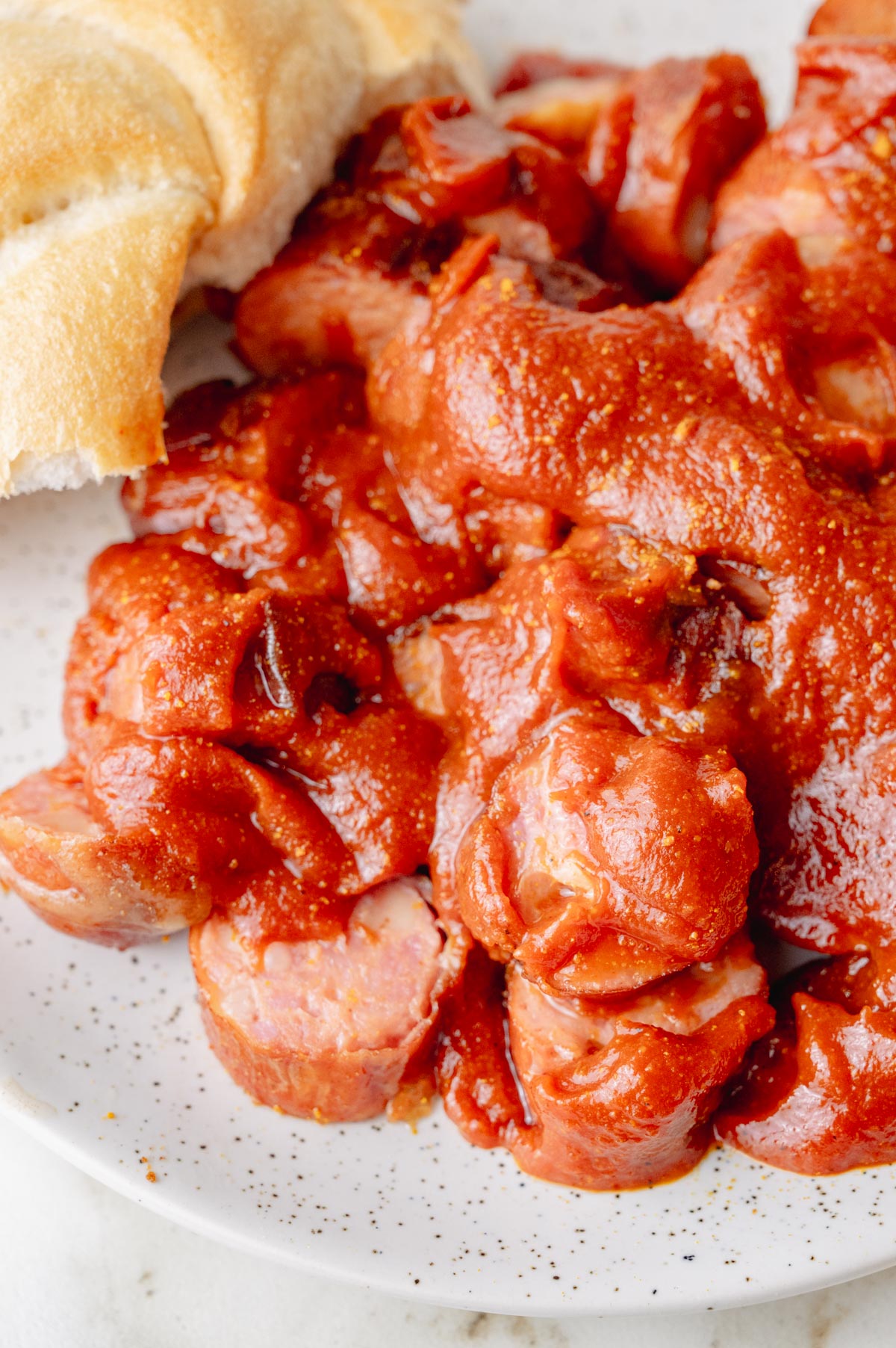 A close-up photo of currywurst with a piece of bread roll on a white plate.