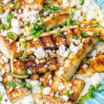 Grilled zucchini with yogurt, pine nuts, basil, and feta on a blue plate.