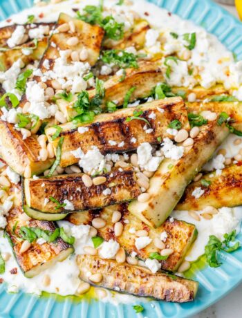 Grilled zucchini with yogurt, pine nuts, basil, and feta on a blue plate.