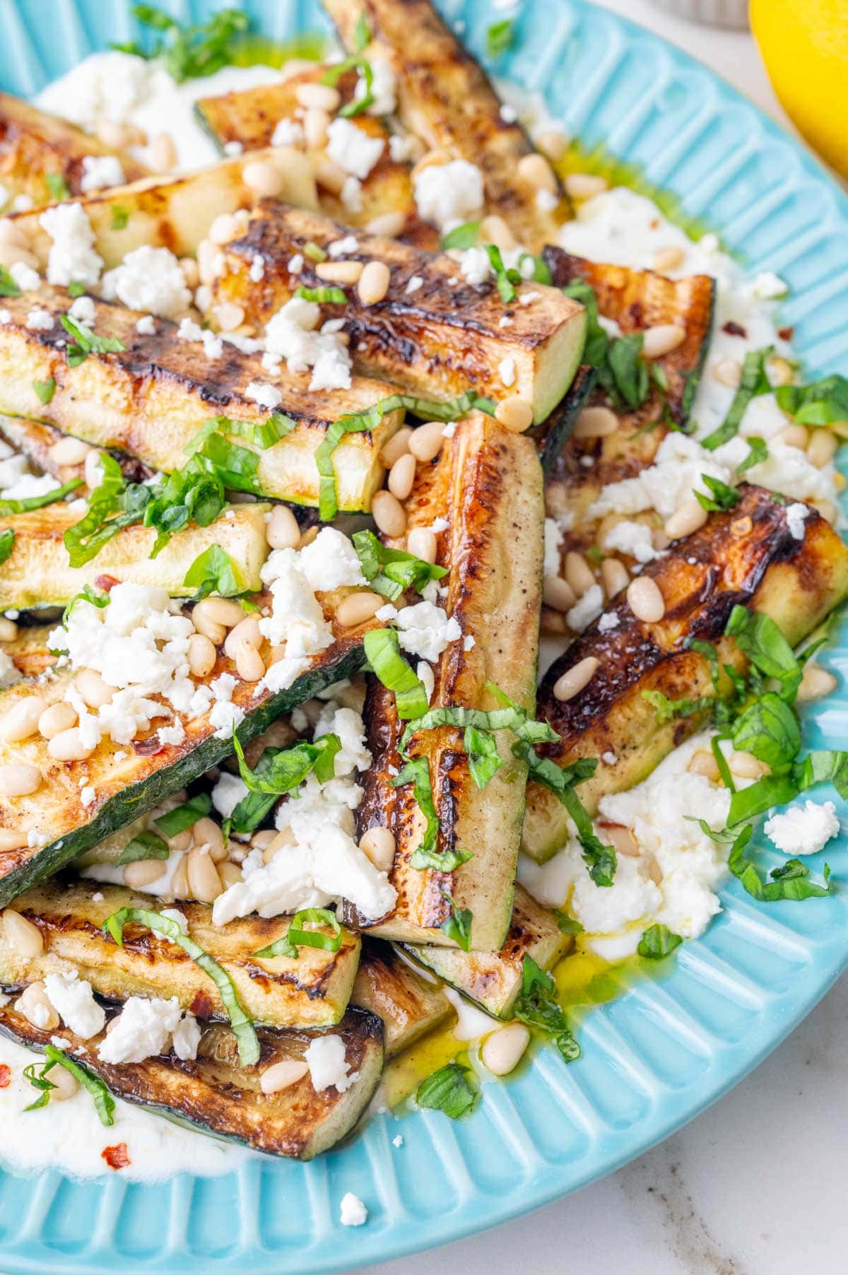 Grilled zucchini with yogurt, basil, pine nuts, and feta on a blue plate.