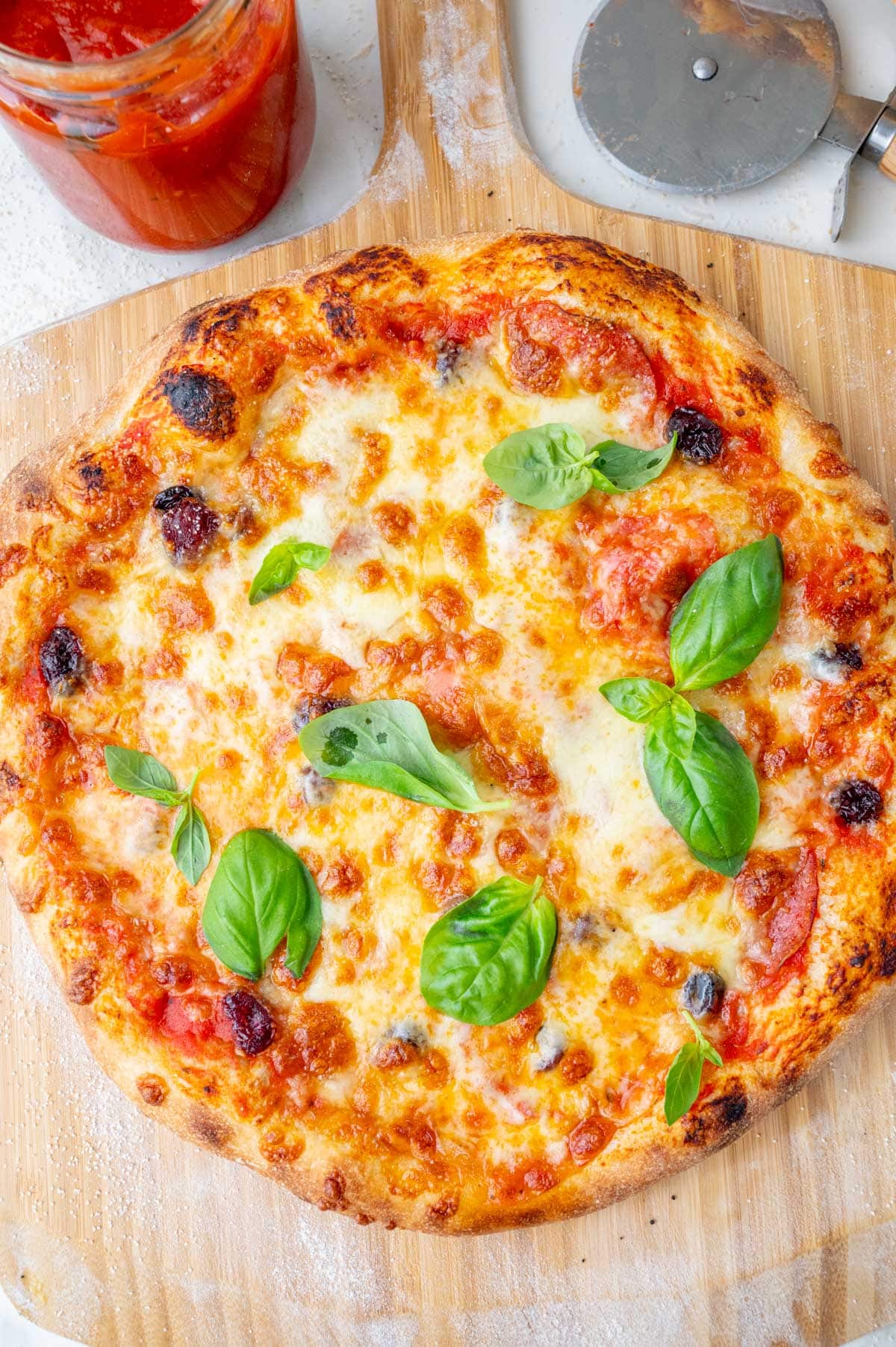 An overhead photo of a pizza topped with cheese, cranberries, chorizo, and basil on a wooden board.