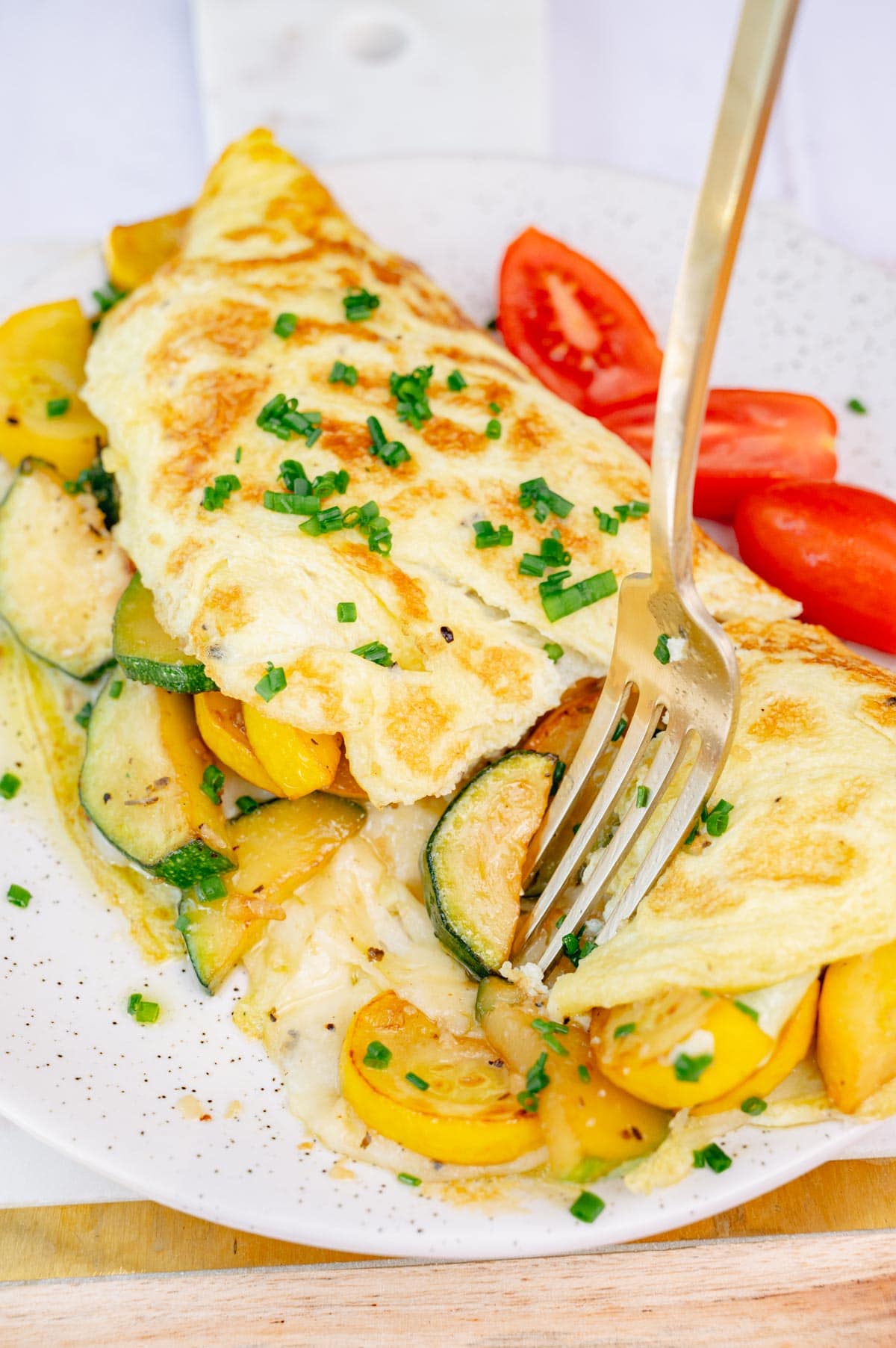 An omelet filled with pan-fried zucchini and melted cheese, topped with chives, on a white plate.