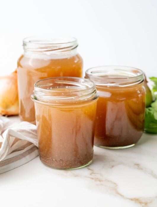 Three jars with beef stock on a marble counter.