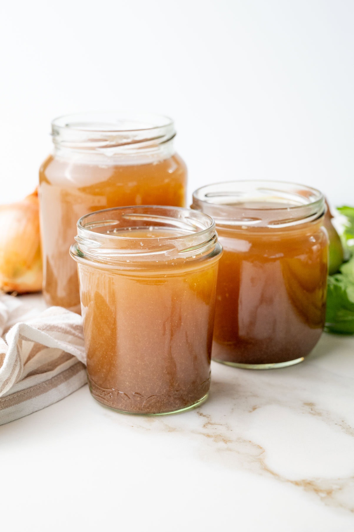 Three jars with beef stock on a marble counter.